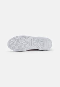 Biała podeszwa sneakersów z teksturowanym wzorem na grip, z małym różowym akcentem. Gładki materiał gumowy o zaokrąglonym kształcie.