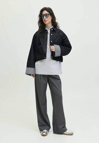Tamna traper jakna skraćena s sivim rukavima, sivi oversized T-shirt, široke sive hlače i metalik mokasine. Odvažne sunčane naočale upotpunjuju izgled.