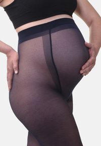 Collants sombres et transparents avec une texture lisse, une taille large et une couture arrière subtile, épousant la jambe et accentuant sa forme.