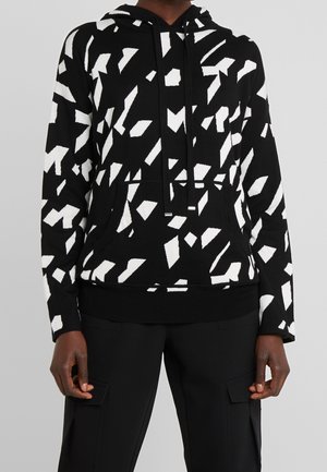 Schwarzer Hoodie mit weißen abstrakten geometrischen Formen, Fronttasche, Kordelzug, getragen mit schwarzen Hosen mit seitlichen Cargotaschen.