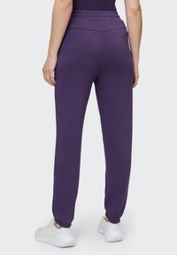 Lila Jogginghose mit schmal zulaufendem Bein, elastischem Bund und weichem Stoff. Kombiniert mit weißen Sportschuhen.