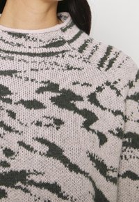Gebreide trui in lichtroze met een donkergroen abstract patroon, voorzien van een hoge hals en een textuurstof in een comfortabele pasvorm.