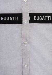 Camicia grigia con bottoni, realizzata in tessuto testurizzato, con righe nere e il testo "BUGATTI" in bianco, e bottoni in plastica trasparente.