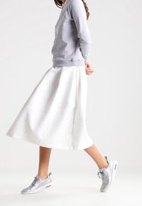 Felpa grigia, gonna A-line bianca e testurizzata, e sneakers argentate. La gonna presenta un motivo dettagliato e arriva sotto il ginocchio.