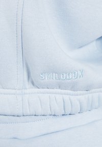 Il tessuto azzurro chiaro presenta una texture liscia con elastico arricciato all'orlo. "SMILOBX" è ricamato in un filo di blu leggermente più scuro.