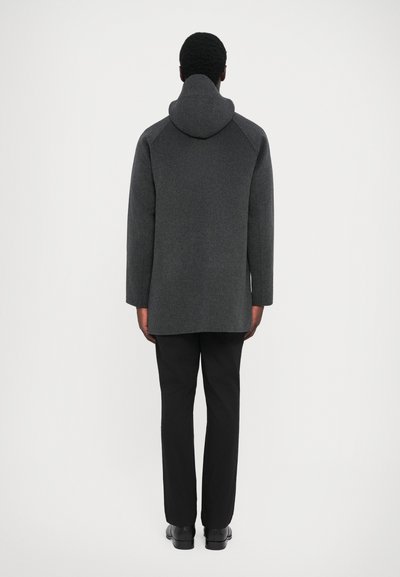 Gray wool coat with hood, featuring a relaxed fit and long sleeves, paired with black trousers and shoes. Back view against a white background.