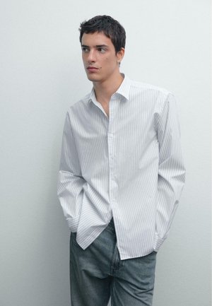 White button-up shirt with light blue vertical stripes, long sleeves, and a classic collar, paired with gray denim pants.