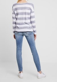 Dlouhý rukáv pruhovaný top v šedé a bílé, spárovaný s světle modrými skinny džíny. K outfitu se hodí volnočasová obuv v bílé barvě.