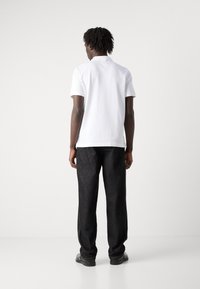 Weißes kurzärmliges Polohemd und dunkle, locker sitzende Jeans. Polierte Schuhe, minimalistisches Design und klare Linien; keine sichtbaren Muster oder Akzente.