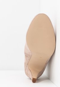 Zapato de tacón alto de ante en beige claro, con punta afilada y suela lisa. Presenta un tacón delgado y un diseño minimalista en los laterales.