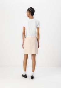 T-shirt branco de manga curta combinado com uma saia de tweed texturizada em tom pêssego, com bainha desfiada, usada com sapatos pretos e meias brancas.