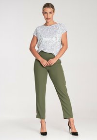 Biała bluzka z krótkim rękawem z wzorem odręcznym, zestawiona z oliwkowymi spodniami w tapered i czarnymi szpilkami. Gładki materiał, luźny krój.