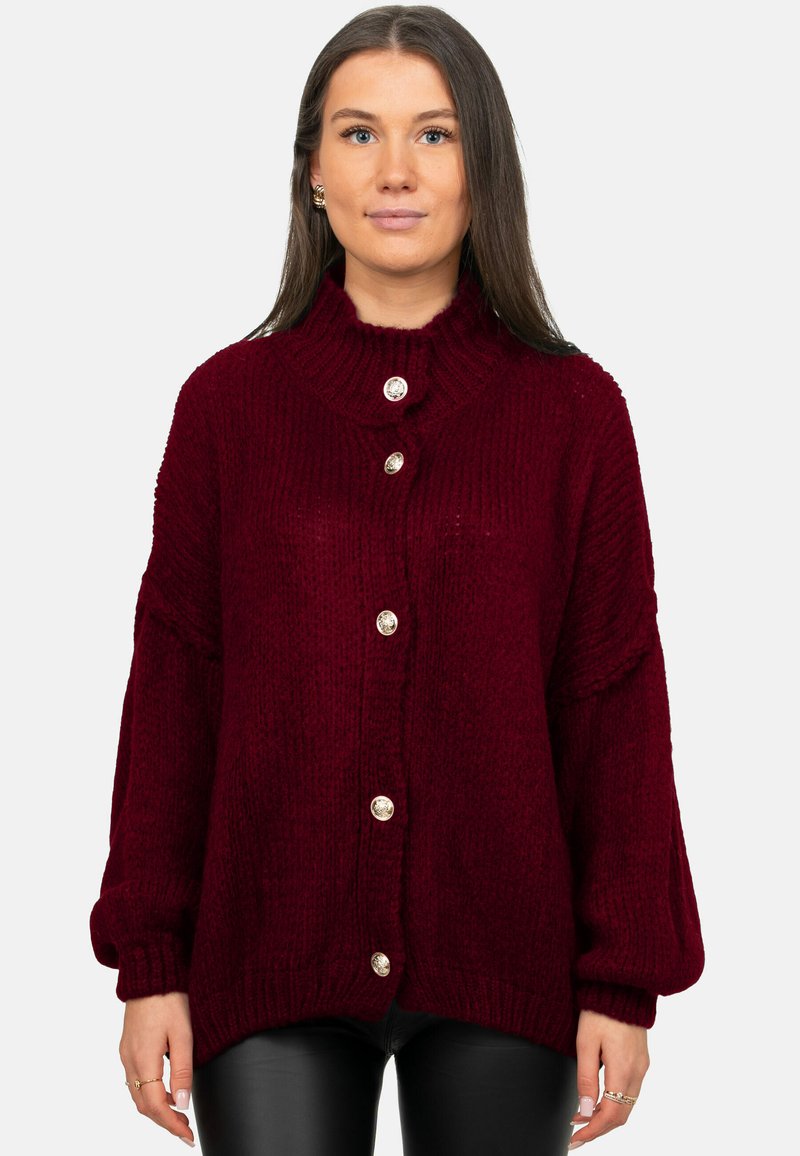 Pull en tricot bordeaux avec col montant, grands boutons argentés, poignets côtelés et silhouette oversize. Tissu texturé au look douillet.