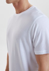 Hvid bomulds t-shirt med rund hals, korte ærmer og en glat tekstur. Har rene syninger langs kanterne og en tætsiddende silhuet.