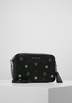 Zwarte leren Michael Kors crossbodytas met zilveren sterrenstuds, kettingriem en kwastdetail op een witte ondergrond.