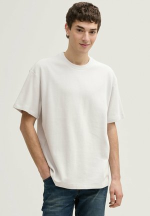 Witte T-shirt met korte mouwen, een ribbelstructuur, een losse pasvorm en een ronde halslijn, gecombineerd met blauwe spijkerbroek.