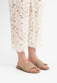 Sandale slide bej, cu vârf deschis, fabricate din suede moale, cu o talpă joasă și o parte superioară care prezintă o curea lată, rotundă.