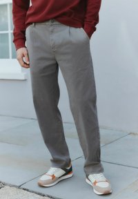 Hellgraue Baumwollhose mit lockerer Passform und Fronttaschen, kombiniert mit mehrfarbigen Sneakers in Orange, Blau und Beige.