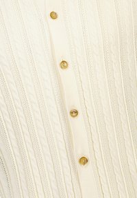 Krämbets stickad tröja med kabelmönster och vertikala ränder, med guldfärgade knappar fram för stängning.