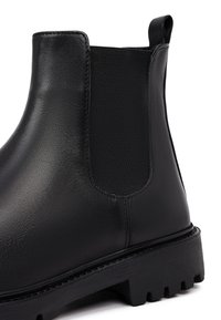 Stivaletto in pelle nera con pannelli laterali elasticizzati, suola nera spessa e cuciture visibili. Caratterizzato da una finitura opaca e un design robusto.