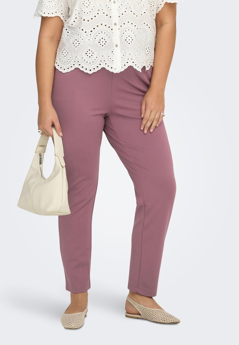 Woman wearing mauve slim pants, white eyelet lace blouse, beige woven slingback flats, holding a small cream handbag.