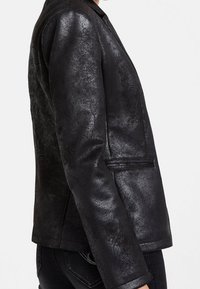 Blazer en simili cuir noir avec un éclat lisse, une forme structurée, une fermeture à un bouton et des poches latérales. Détails de finition texturée visibles.