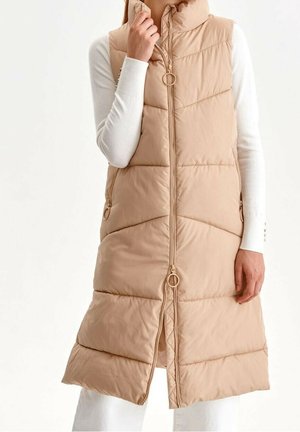 Beige puffer vesta s vysokým límcem, vertikálním prošíváním, předním zipem a zlatými kovovými detaily. Obsahuje boční kapsy.
