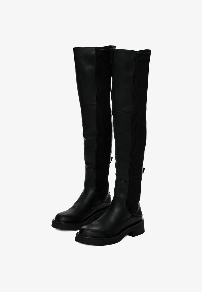 Černé kozačky nad kolena s hladkou kůží, žebrovanými textilními panely, plochými podrážkami a širokým, strukturovaným tvarem.