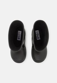Bottes en caoutchouc noires avec un extérieur lisse, une doublure en néoprène, des orteils ronds et un talon légèrement surélevé. Présente une étiquette de logo à l'intérieur.