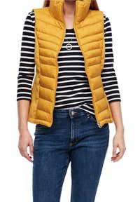 Żółta kamizelka puchowa z wysokim kołnierzem, z przodu na zamek, o pikowanym wzorze, noszona na czarno-białą koszulę z d�ługim rękawem w paski.