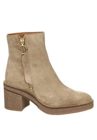 Bottine en daim beige avec talon bloc et fermeture éclair dorée ornée d'une languette circulaire sur le côté extérieur.