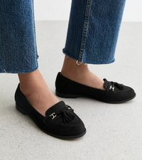Mocasines de ante negro con un acento de borlas y un herraje decorativo, con suela plana y punta redondeada, combinados con pantalones de mezclilla cortos.