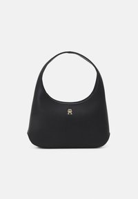 Czarna torebka z ekoskóry o zaokrąglonym kształcie i pojedynczym pasku na ramię. Z przodu złote logo jako ozdoba. Gładka faktura.