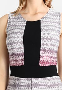 Bezramenné šaty s geometrickým vzorem v odstínech šedé a růžové, s pevným černým panelem uprostřed a přiléhavým, strukturovaným pasem.