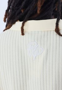 Prenda de manga larga ribeteada de color amarillo claro con una textura suave y logo bordado en blanco en la parte posterior.