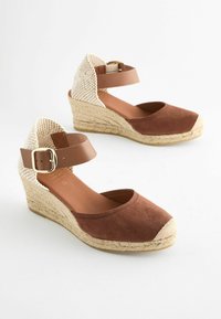 Scarpe con zeppa in suede marrone con un retro intrecciato chiaro, cinturino alla caviglia regolabile e suola avvolta in juta. Design con punta rotonda e texture liscia.