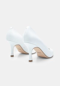 Fehér magas sarkú pumpák sima bőr külsejével, hegyes orral és 7 cm-es tűs sarkával. Diszkrét logó az insole-on.