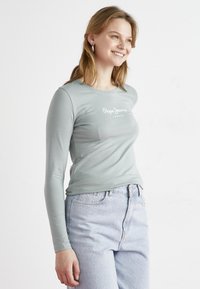 Šviesiai žalia ilgomis rankovėmis marškinėliai su apvaliu iškirpimu ir balta "Pepe Jeans London" logotipu. Derinama su šviesiai mėlynomis aukštu juosmeniu džinsais.
