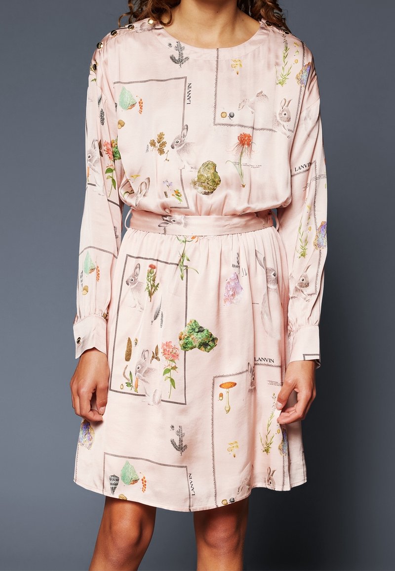 Robe rose à manches longues avec poignets boutonnés et imprimés inspirés de la nature représentant des lapins, des fleurs et des plantes encadrés dans des contours rectangulaires.