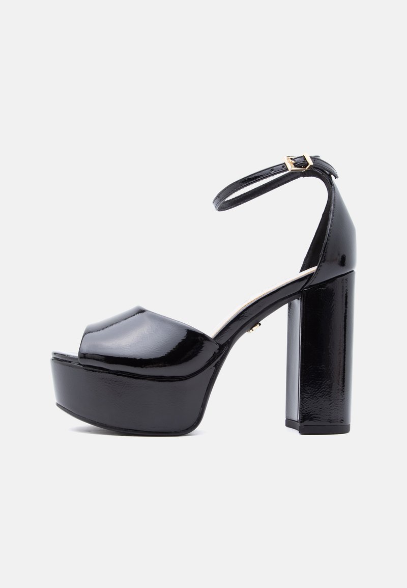 Μαύρο πλατφόρμα σανδάλι από λουστρίνι με χοντρό ψηλό τακούνι και λουράκι αστραγάλου με χρυσή αγκράφα, εμφανίζεται από πλευρά σε λευκό φόντο.