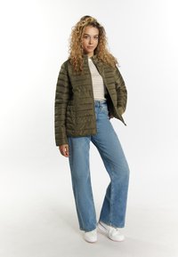 Oliven grøn polstret jakke med lodrette stikninger, båret over en stribet top og parret med vidde bukser i blå denim og hvide sneakers.