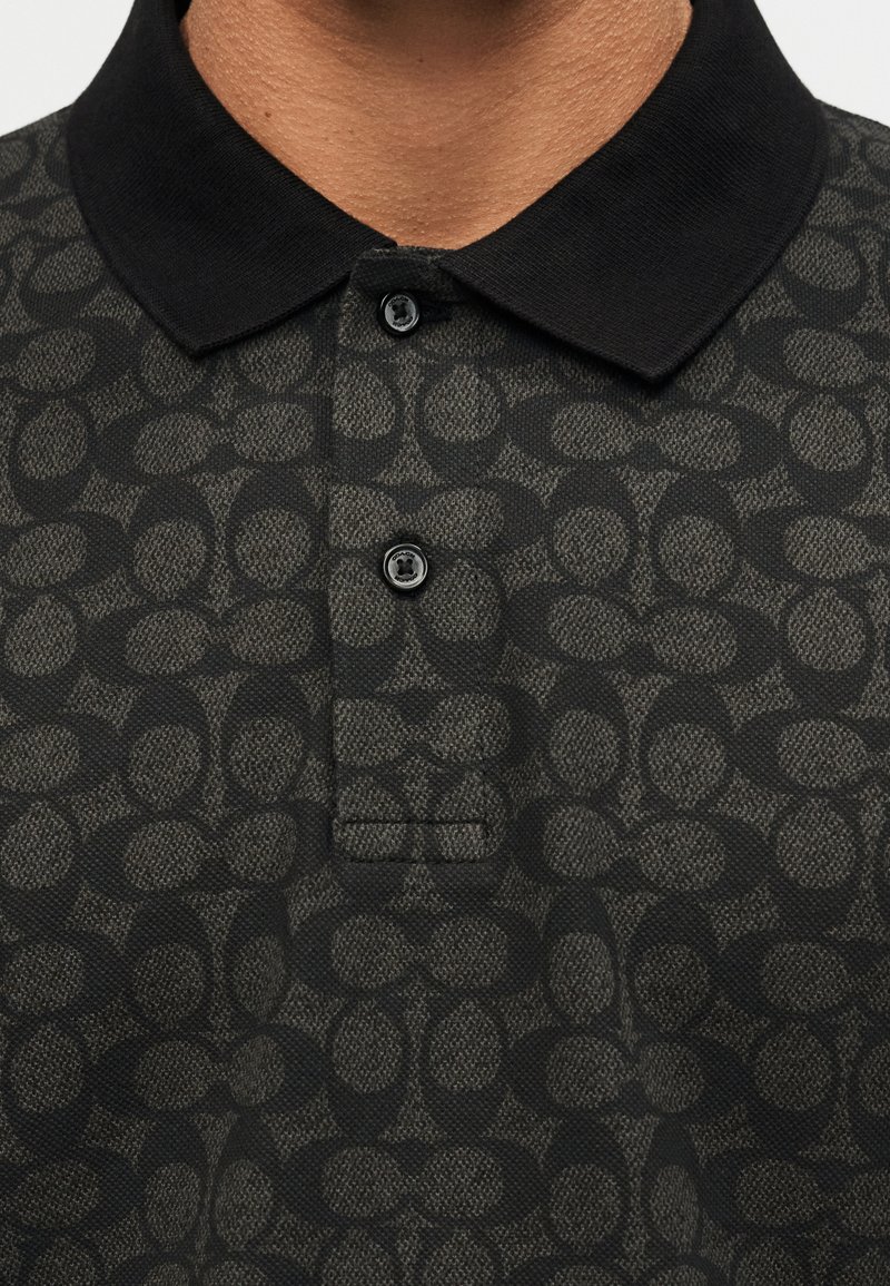 Black polo shirt with a textured, circular pattern and two black buttons at the collar, worn by a person with medium brown skin.