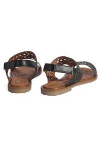 Schwarze Ledersandalen mit durchlöchertem Design, braunen Innensohlen, Fersenriemen und flachen, tanfarbenen Sohlen. Offene Zehenform für Atmungsaktivität.