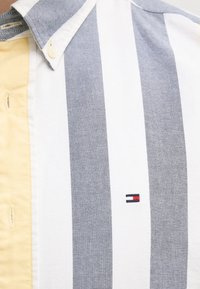 Camisa de manga corta con rayas alternas en azul oscuro y blanco, con un panel amarillo. Logotipo bordado en el pecho. Material de mezcla de algodón.