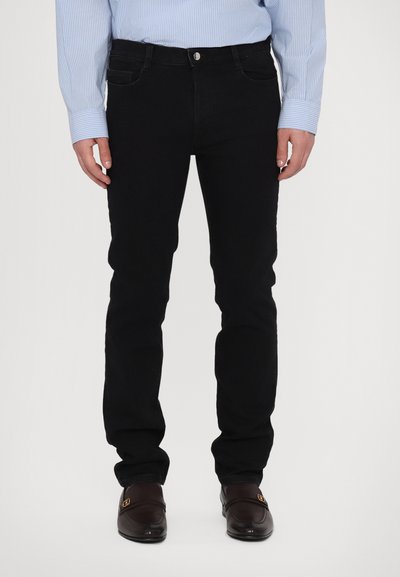 Sorte denimjeans med slim fit, der har en frontknaplukning, bæltestropper og diskrete lommeoplysninger. Stylet med en lyseblå stribet skjorte.