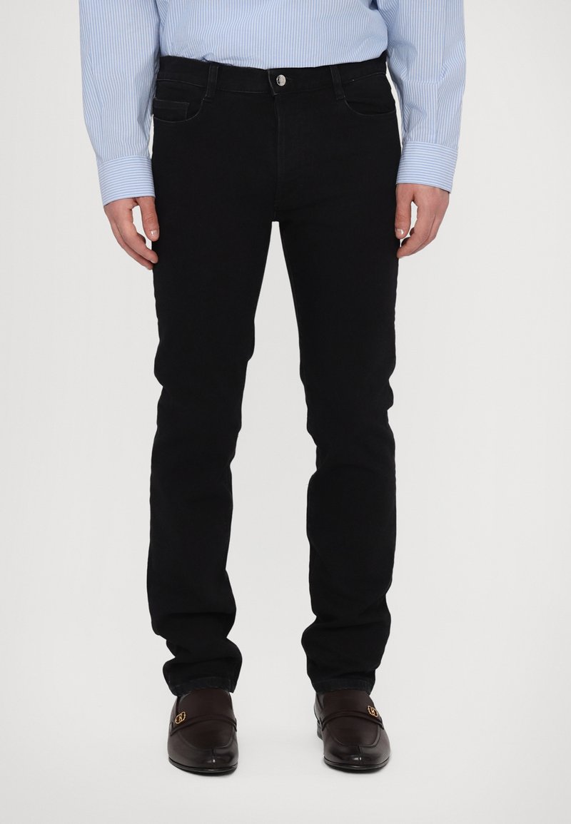 Mustad denim teksad, mis on kitsas sobivusega, esise sulepingutusega, vöödega ja diskreetsete taskudetailidega. Kombineeritud helesinise triibulise särgiga.