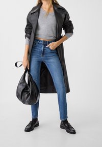 Musta nahkainen trenssitakki, harmaa lyhyt neulepaita, siniset korkeavyötäröiset farkut, mustat loaferit ja musta rento käsilaukku. Näytetään sileit�ä tekstuureja.