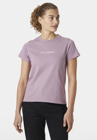 Camiseta de algodón morado claro con mangas cortas, que presenta un logo impreso en blanco "HELly HANSEN" centrado en el pecho, combinada con pantalones negros.