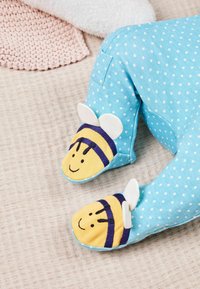 Blaue Hausschuhe mit weißen Punkten und gelben, bienenförmigen Zehenschutzkappen, die bestickte Gesichter und weiße Stoffflügel haben. Aus weichem Stoffmaterial.