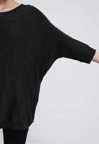 Maglione nero largo con maniche tre quarti, colletto e polsini a coste, realizzato in un morbido tessuto testurizzato.